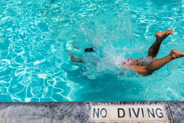 Jemand springt in einen Pool, an dessen Rand ein Schild steht, auf dem "no diving", also "springen verboten" steht